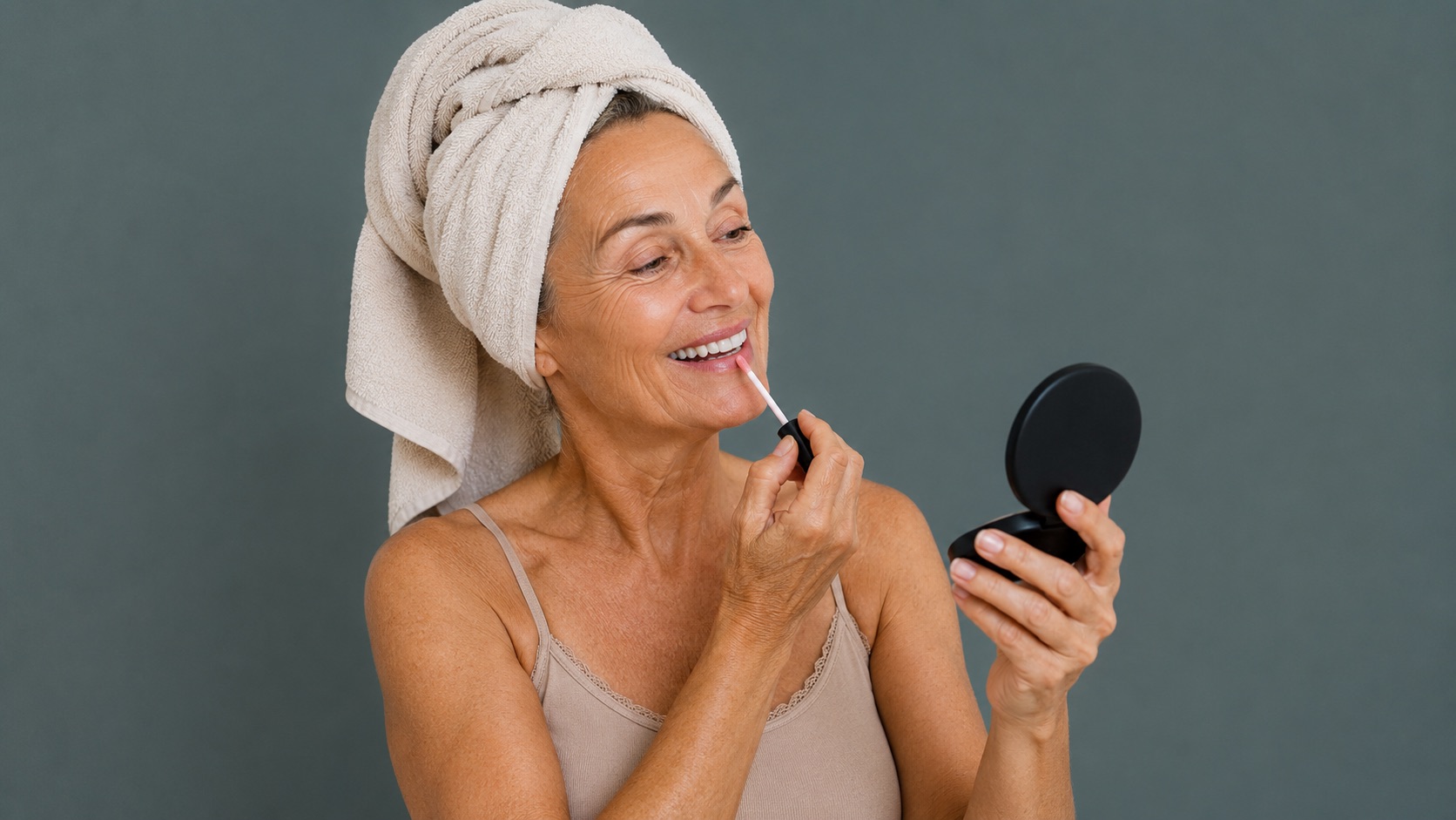 Ältere Frau mit Handtuchturban trägt vor einem kleinen Spiegel Lipgloss auf