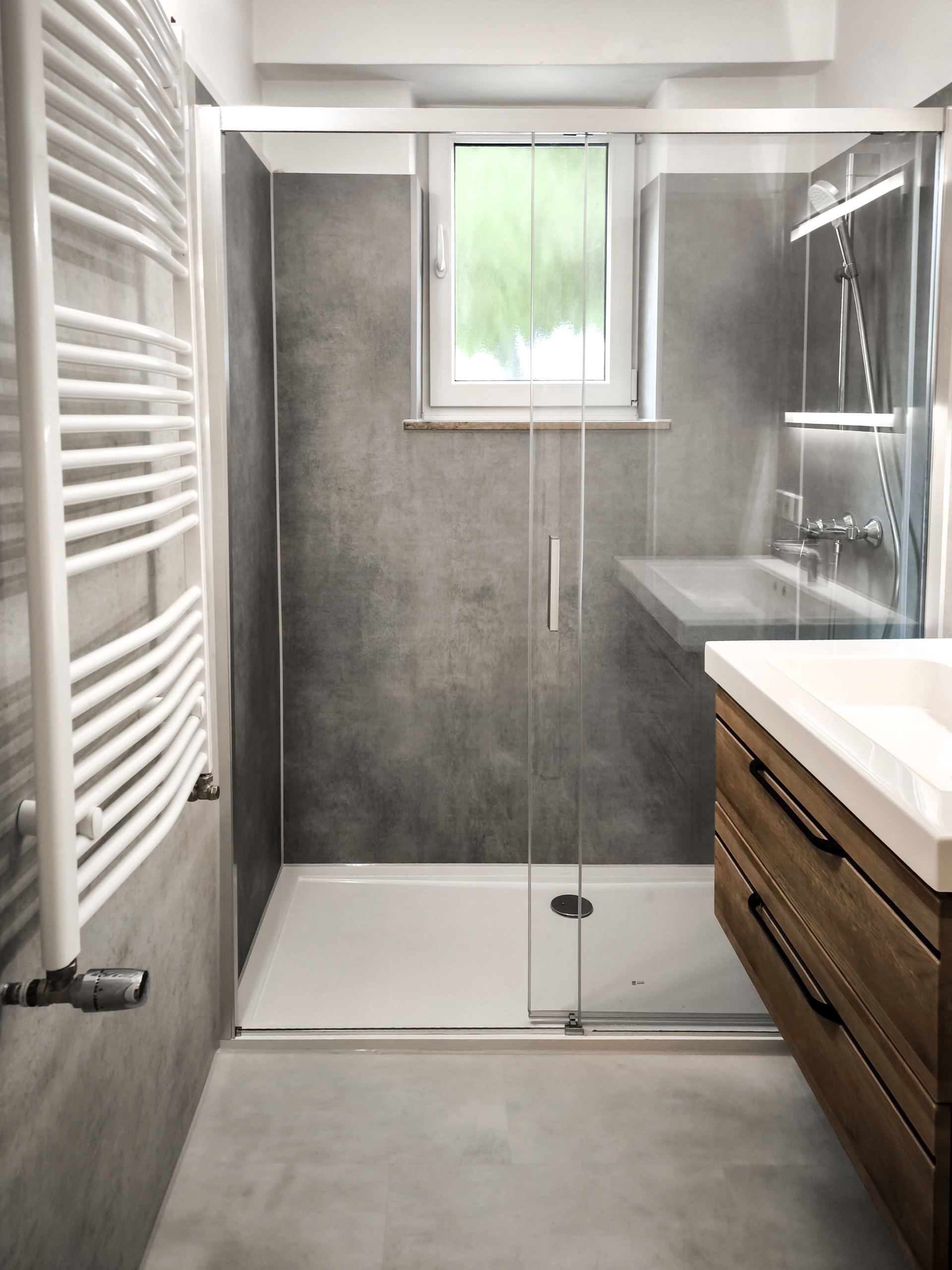 Dusche mit Schiebetür vor dem Fenster und Waschtisch in Holzoptik