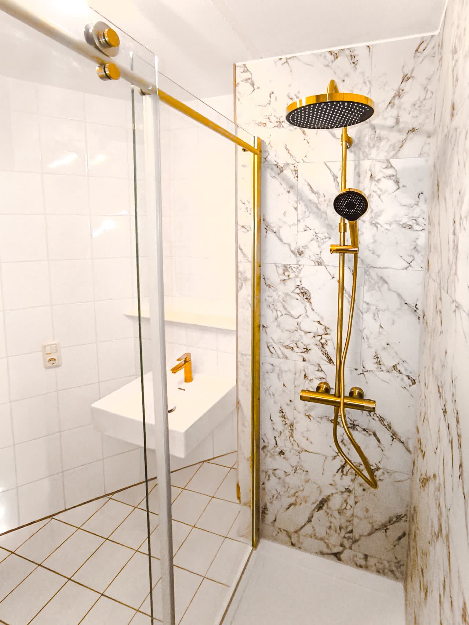 Regendusche in Messing vor einer Wand in heller Marmoroptik